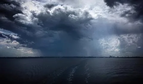 Dark storm clouds over a calm water body on a cloudy day Stock Photos