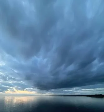 Dark storm clouds over calm water with a cloudy sky Stock Photos