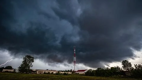 Dark storm clouds over a cell tower with lightning nearby Stock Photos