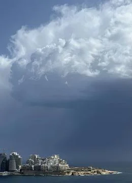 Dark storm clouds over city buildings near the coast Stock Photos