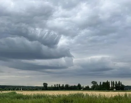 Dark storm clouds over a green field and trees Stock Photos