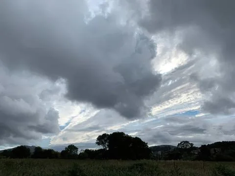 Dark storm clouds over a green field with trees and hills Stock Photos
