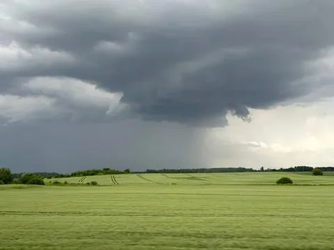 Dark storm clouds over green fields on a cloudy day Stock Photos