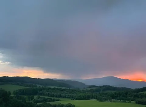 Dark storm clouds over green landscape at sunset Stock Photos