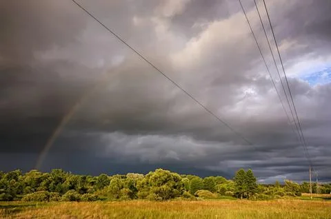 Dark storm clouds over green field with power lines Stock Photos