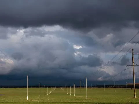Dark storm clouds over green field with power lines Stock Photos