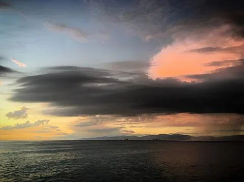 Dark storm clouds over ocean at sunset with colorful sky Stock Photos