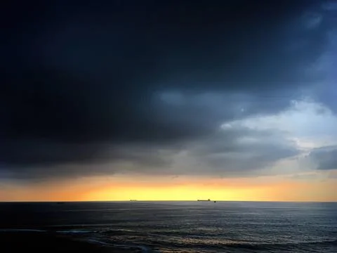 Dark storm clouds over ocean with sunset sky in the background Stock Photos