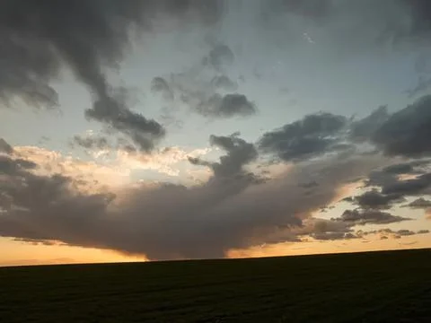 Dark storm clouds over open field during sunset sky Stock Photos