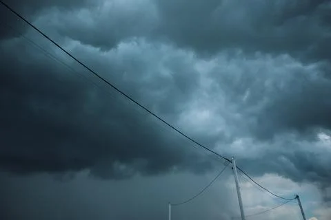 Dark storm clouds over power lines and electrical poles low angle view Stock Photos
