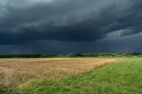 Dark storm clouds over the stubble and meadow Stock Photos