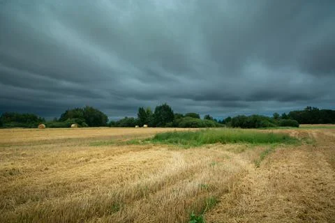 Dark storm clouds over stubble field, summer day Stock Photos