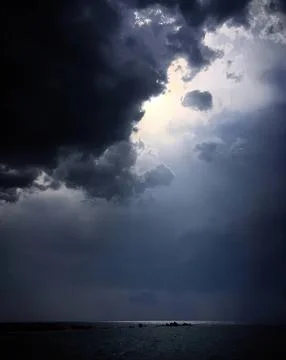 Dark storm clouds over water with bright sunlight breaking through Stock Photos