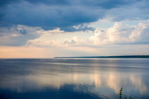 Dark storm clouds over wide reservoir at sunset with soft sunlight reflection Stock Photos