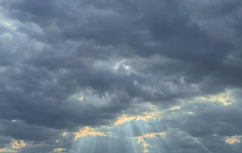 Dark storm clouds part as bright sunrays break through the sky, creating a po 스톡 사진