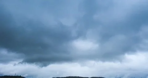 Dark storm clouds rolling in overcast skies over a distant forested hill Stock Footage 342015906