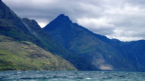 Dark stormy mountain peak towering above blue alpine lake Stock Footage 159749795