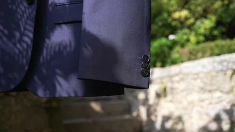 Dark suit jacket hanging outdoors near stone wall Vídeos de archivo 331049073