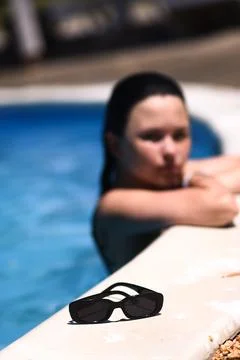 Dark sunglasses lie on border while blurred woman relaxes inside swimming poo Stock Photos