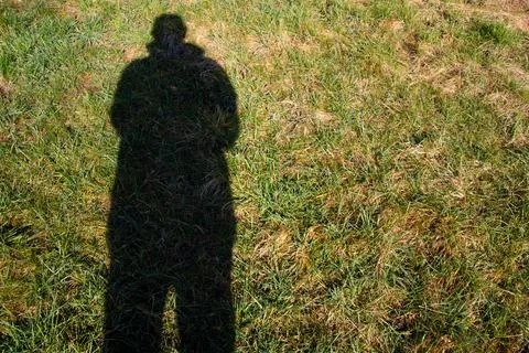 Dark tall shadow of a man with coat in the grass Stock Photos