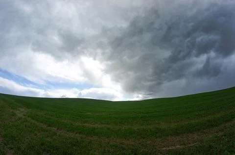 Dark thundercloud approaching the blue sky over the green field Stock Photos