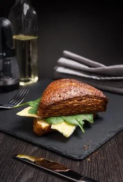 Dark triangular sandwich with cheese and greens on a black board. Stock Photos