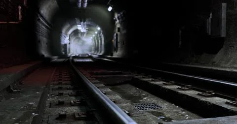 Dark underground tunnel with train tracks illuminated by distant lights Illustrazione stock
