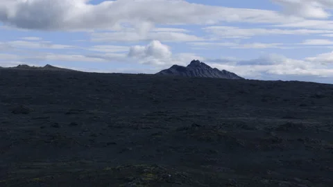 Dark volcanic lava field with distant rocky peak Stock Footage 319280005