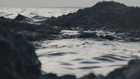 Dark volcanic rocks emerge from the cold choppy ocean waves. Stock Footage 337412841