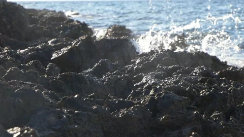 Dark volcanic rocks stand strong against splashing blue ocean waves Stock Footage 337411419