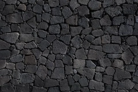 Dark volcanic stone wall texture with irregular pattern Stock Photos
