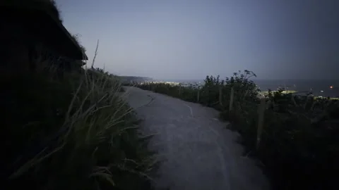 Dark walking path towards seaside town panning Stock Footage 340195347