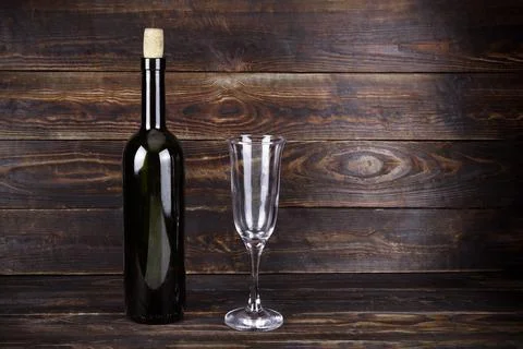 Dark wine bottle and empty transparent wineglass on brown wooden background Stock Photos