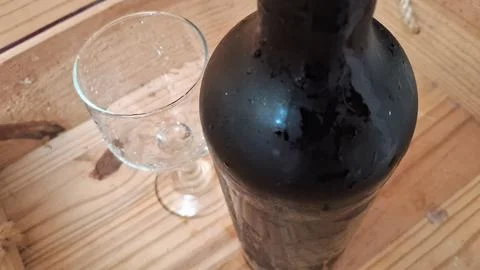 Dark wine bottle and empty glass resting on wooden surface 库存照片