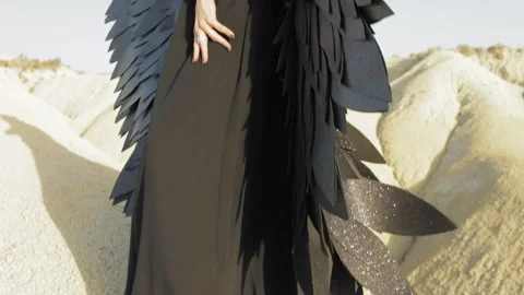 Dark-winged angel standing barefoot on barren ground, black dress billowing.. Stock Footage 311669879