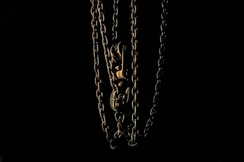 Darkness. A metal chain with a hook hangs from the ceiling, illuminated by a  Stock Photos