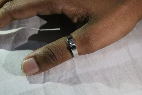 A darkskinned hand with a silver ring on the index finger resting on a whit.. Fotos Stock