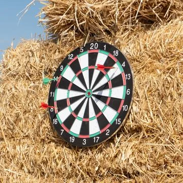 A dartboard on a haystack with several darts hitting and missing Foto stock