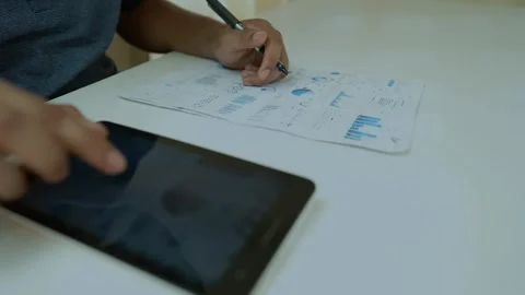 Data Analysis with Charts and Tablet, Person analyzing data charts on paper.. Stock Footage 318578309