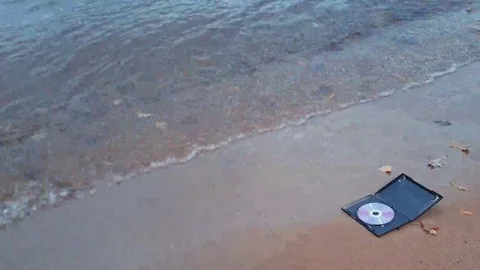 Data cd disc in fire on the sand at coast Stock Footage 69156382