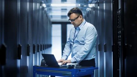 In Data Center IT Engineer Works on Crash Cart Laptop. We See Rows of Server  Stock Photos