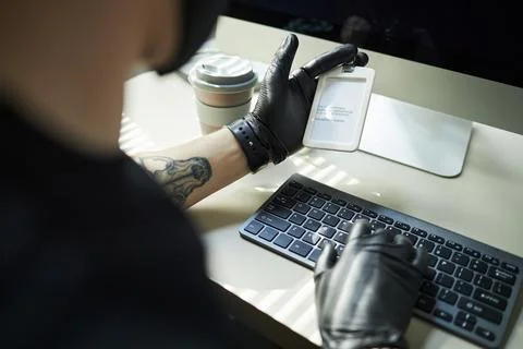 Data Thief in Gloves Holding ID Card while Hacking Computer in Office 库存照片
