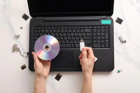 Data transfer and storage solutions: hands holding CD and USB drive over lapt 库存照片