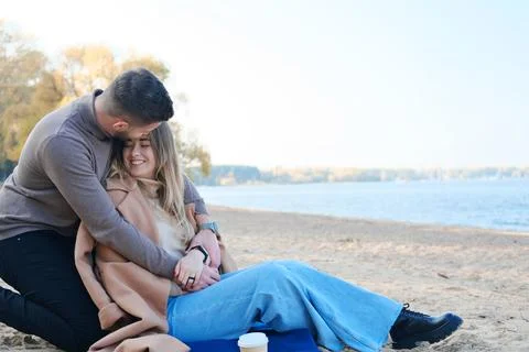 Date on the beach in the cold season. The guy hugs the girl from behind by th Stock Photos