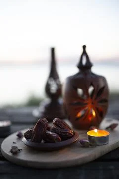 Dates and a candlelit lantern on a wooden board by the sea at dusk Stock Photos