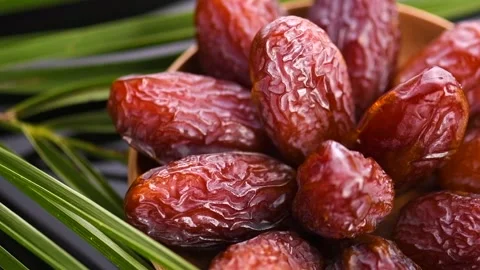 Dates fruit. Date fruits with palm tree leaf, in a wooden bowl, on black Stock Footage 281560463