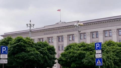 Daugavpils University main building facade with Latvian flag and green trees Stock Footage 344355198