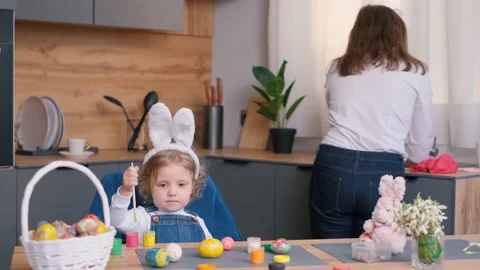 The daughter is busy coloring eggs for Easter, and the mother is washing dishes Video stock 236223267
