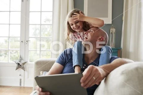 Daughter on dads shoulders, using a tablet together at home Stock Photos