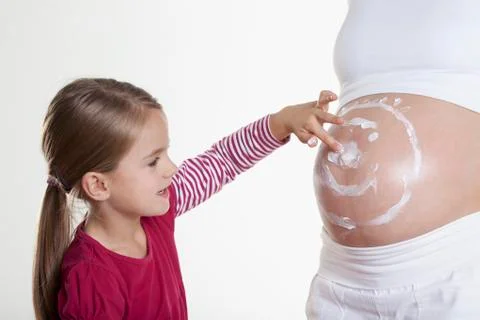Daughter drawing smiley face on stomach of her pregnant mother Stock Photos